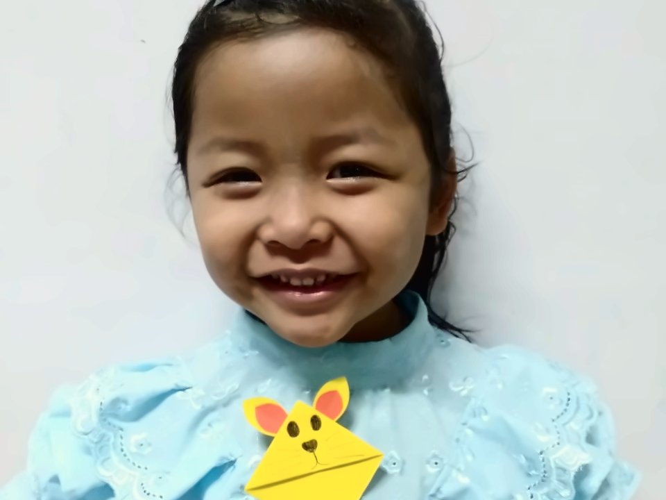 เด็กหญิงในชุดไทยยิ้มพร้อมงานพับกระดาษรูปกระต่ายฝีมือตัวเอง