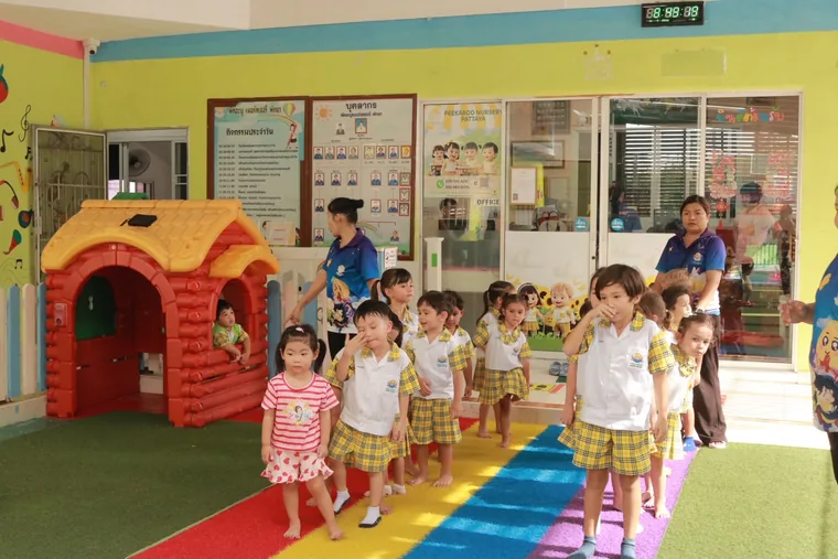 เด็กและคุณครูในลานเล่นสีรุ้งที่มีบ้านจำลองและเครื่องเล่น