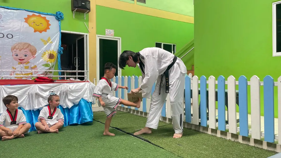 เด็กฝึกเตะเป้าเทควันโดกับครูผู้ฝึกสอน โดยมีเพื่อนรออยู่ข้าง ๆ