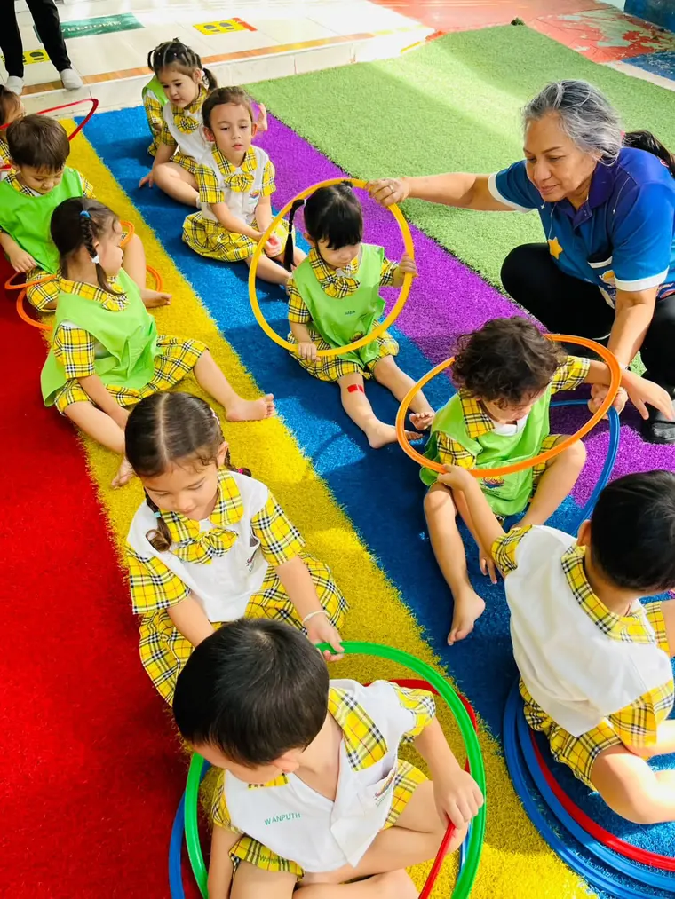 คุณครูช่วยเด็ก ๆ เล่นส่งห่วงเป็นกลุ่มบนสนามสีรุ้ง