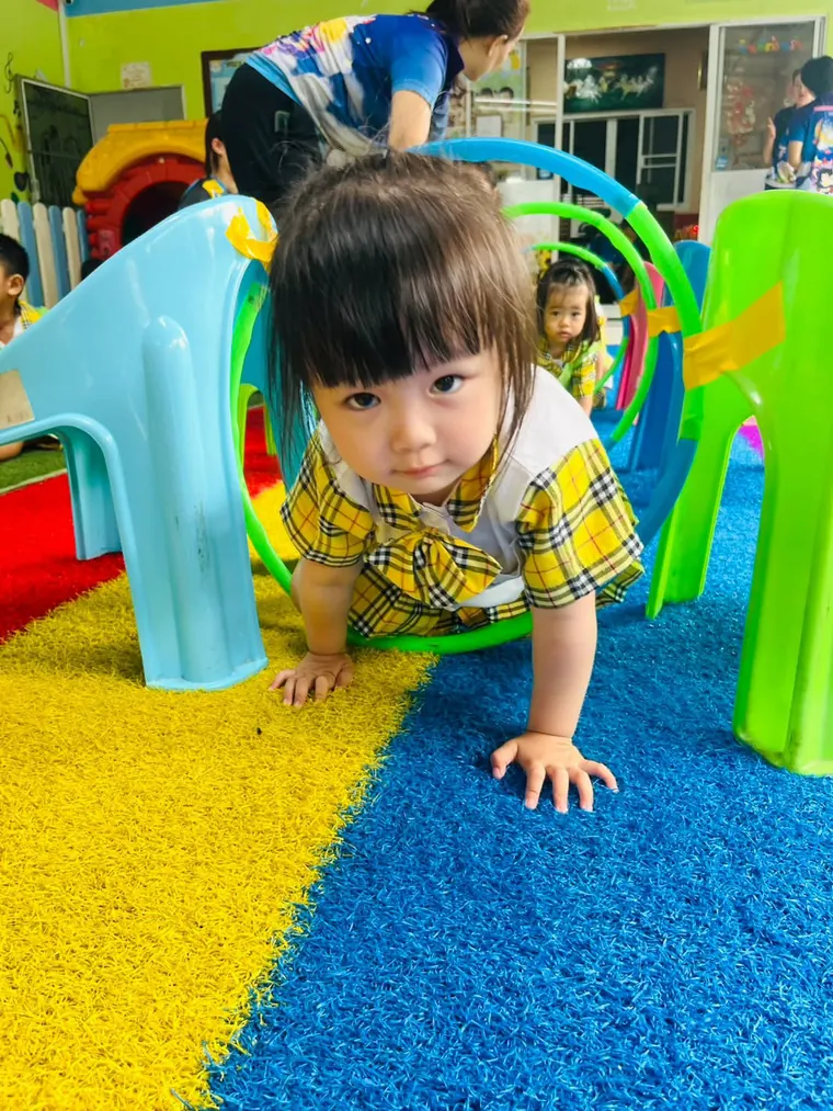 เด็กในชุดพีคอะบูคลานผ่านอุโมงค์ของเล่นสีฟ้าและเขียว