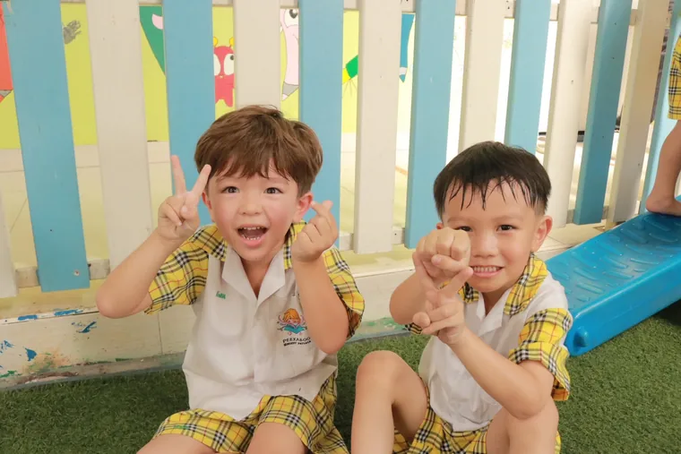 เด็กสองคนยิ้มและทำมือทักทายขณะนั่งข้างกัน
